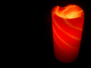 [A red pillar candle burning in the darkness]